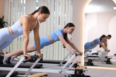 Photo of Woman and pilates instructor exercising on reformers in studio