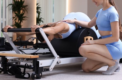Photo of Woman exercising on reformer supervised by pilates instructor in studio