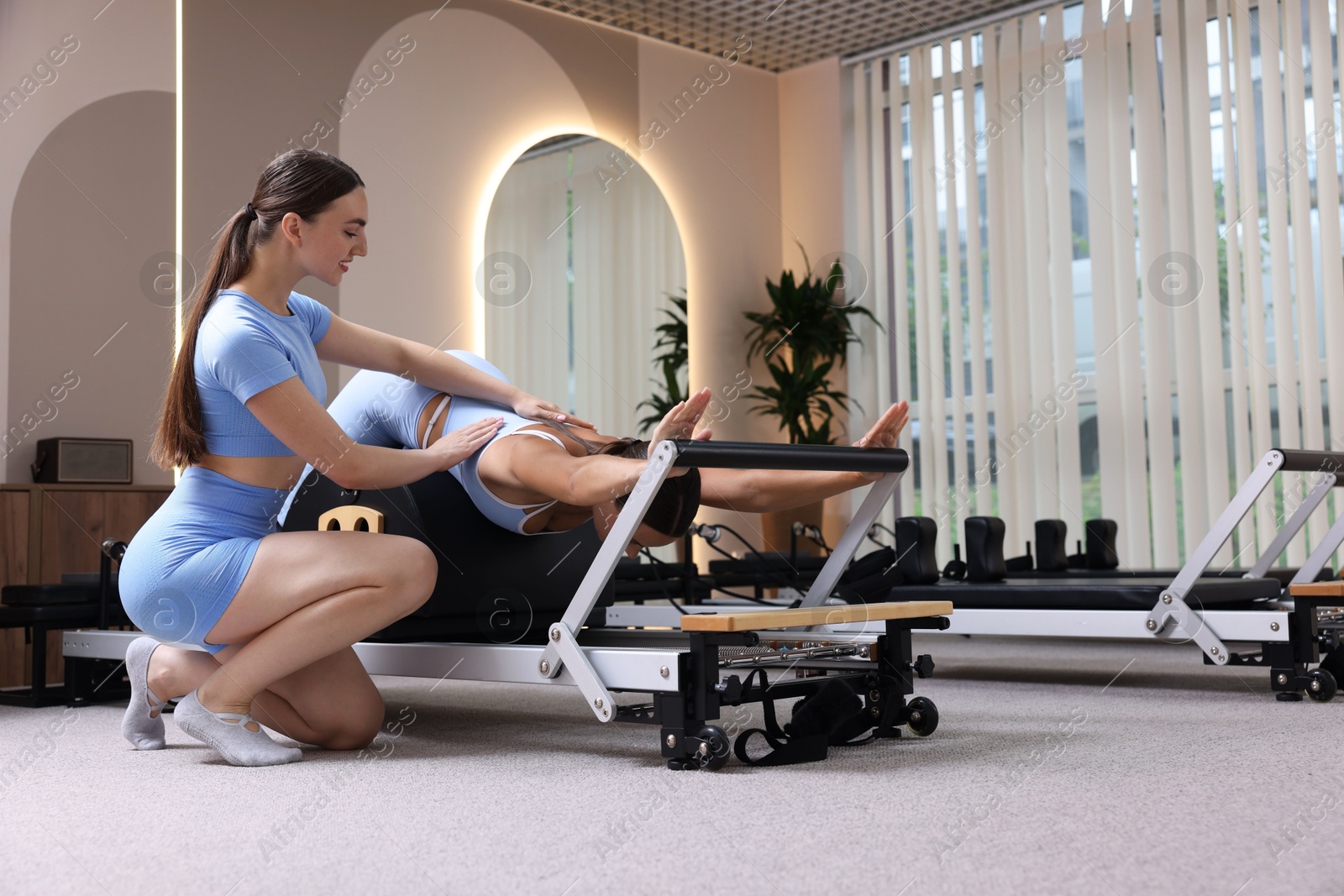 Photo of Woman exercising on reformer supervised by pilates instructor in studio