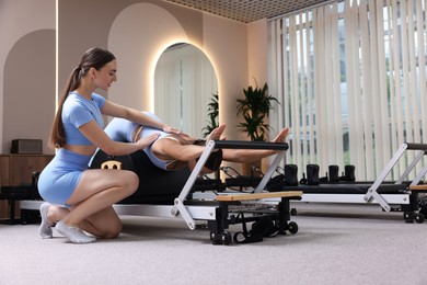 Photo of Woman exercising on reformer supervised by pilates instructor in studio