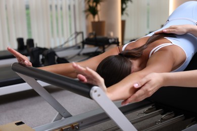 Photo of Woman exercising on reformer supervised by pilates instructor in studio
