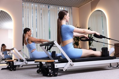 Photo of Woman and pilates instructor exercising on reformers in studio