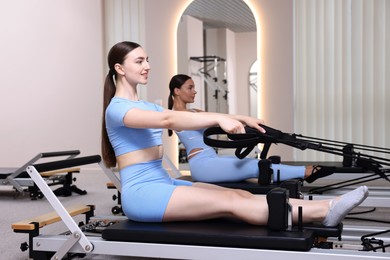 Photo of Woman and pilates instructor exercising on reformers in studio