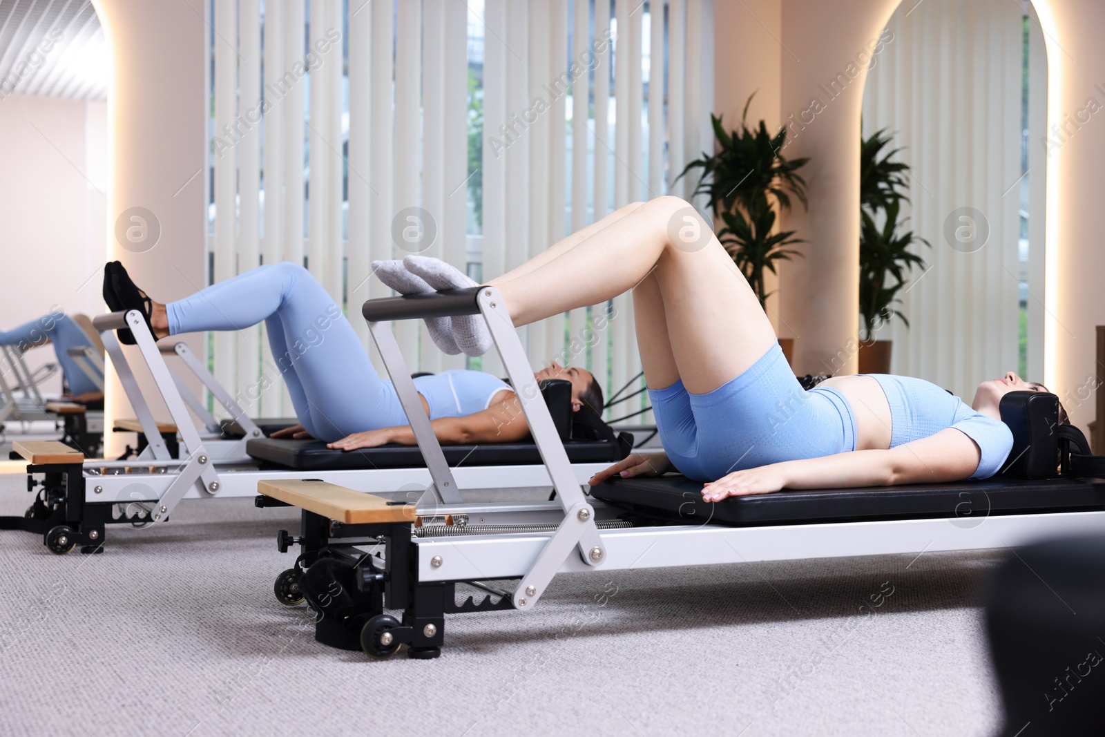 Photo of Woman and pilates instructor exercising on reformers in studio