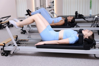 Photo of Woman and pilates instructor exercising on reformers in studio