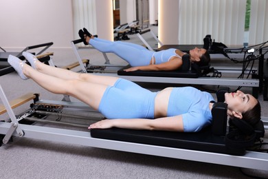 Photo of Woman and pilates instructor exercising on reformers in studio