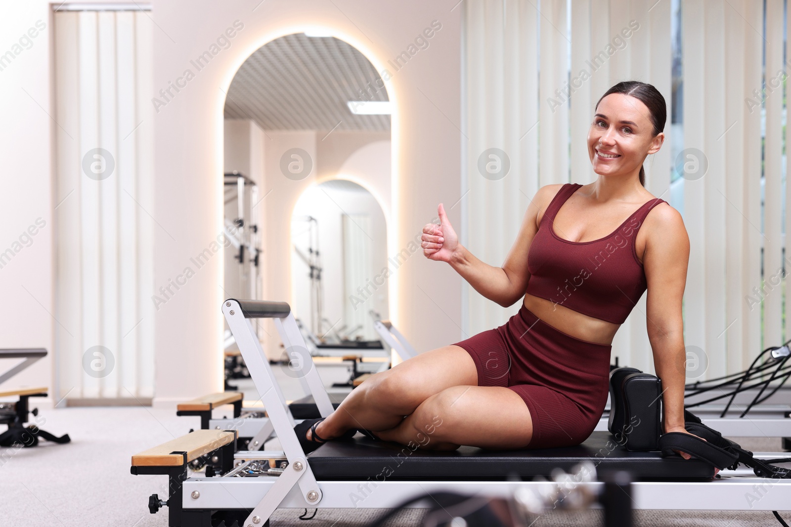 Photo of Happy woman showing thumbs up on reformer in pilates studio