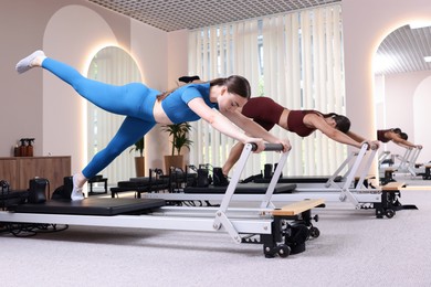 Photo of Woman and pilates instructor exercising on reformers in studio