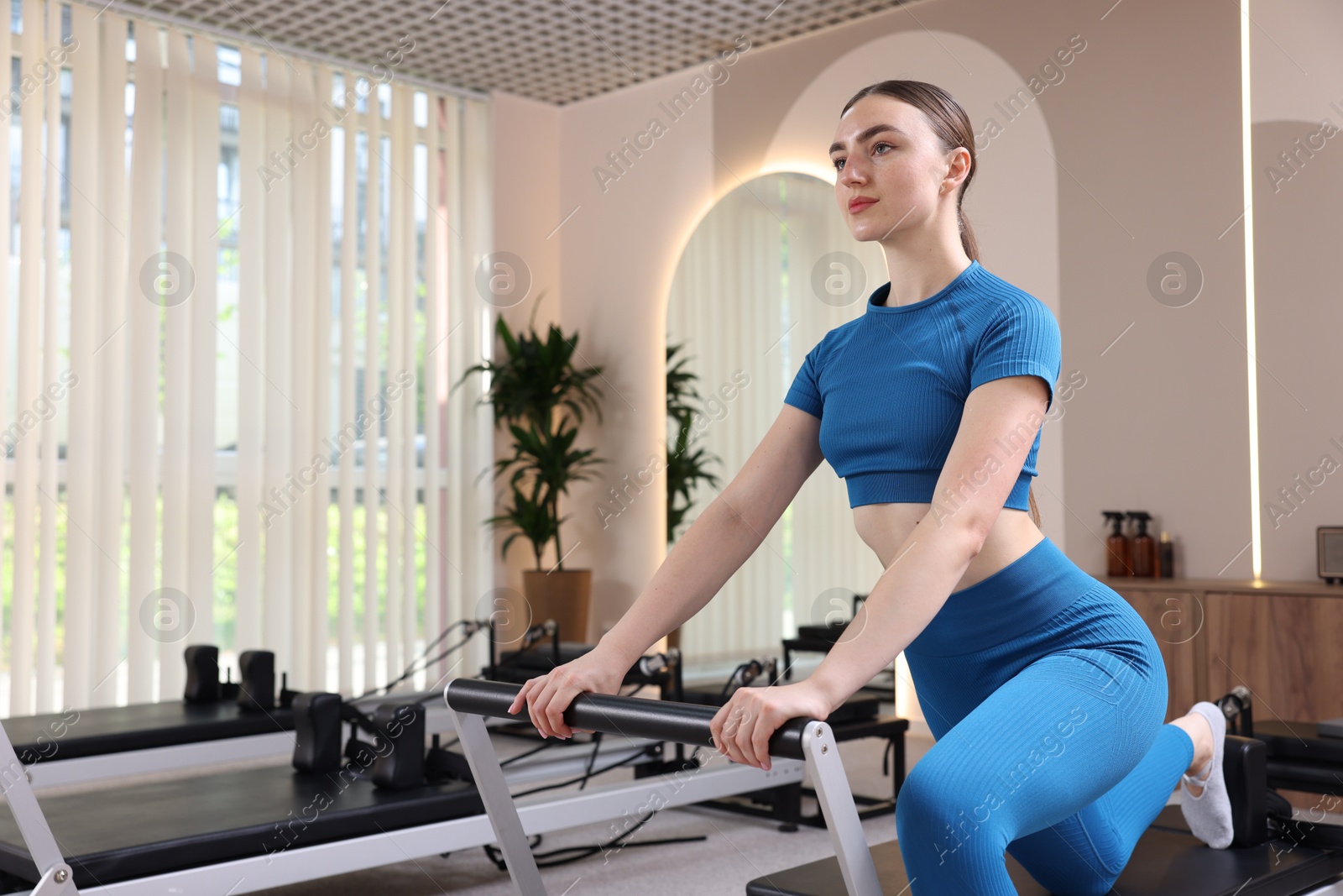 Photo of Woman exercising on reformer in pilates studio, space for text