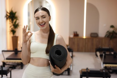 Photo of Woman with fitness mat showing ok gesture in pilates studio, space for text