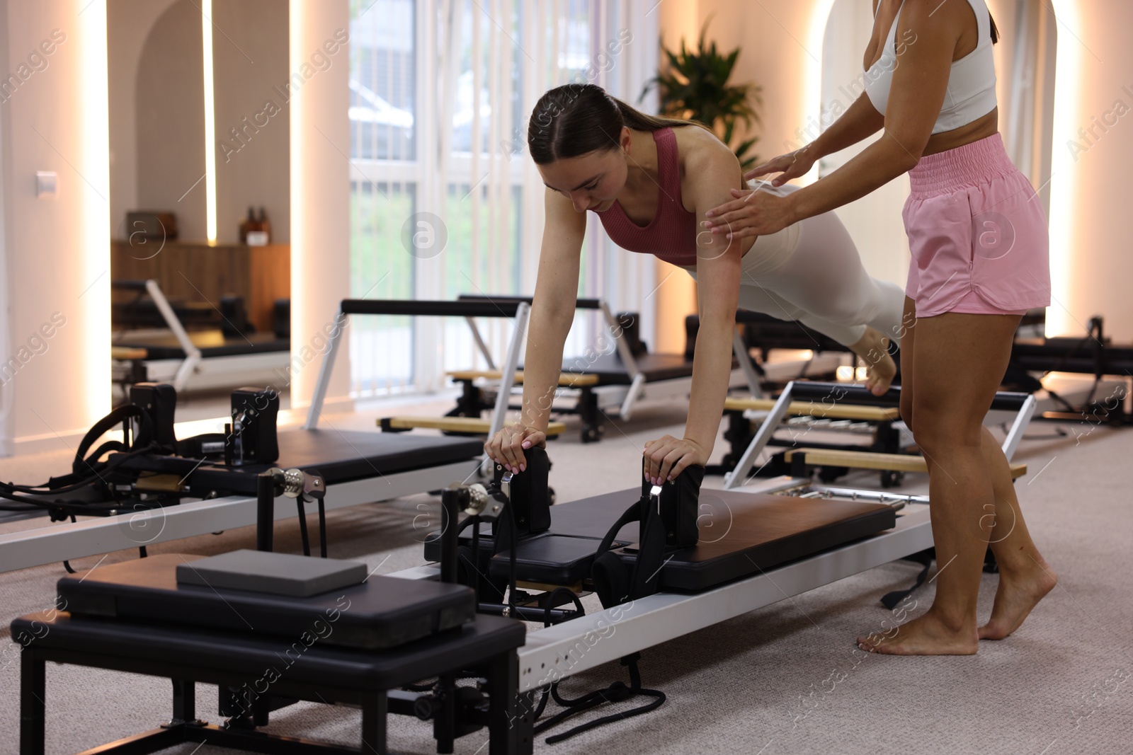 Woman exercising on reformer supervised by pilates instructor in studio Photo of Woman exercising on reformer supervised by pilates instructor in studio