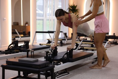 Photo of Woman exercising on reformer supervised by pilates instructor in studio