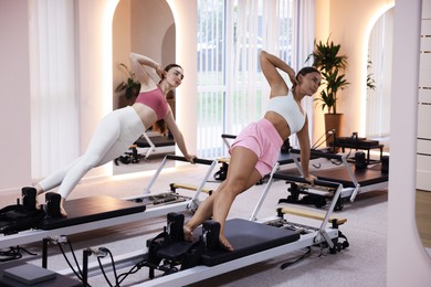 Photo of Woman and pilates instructor exercising on reformers in studio