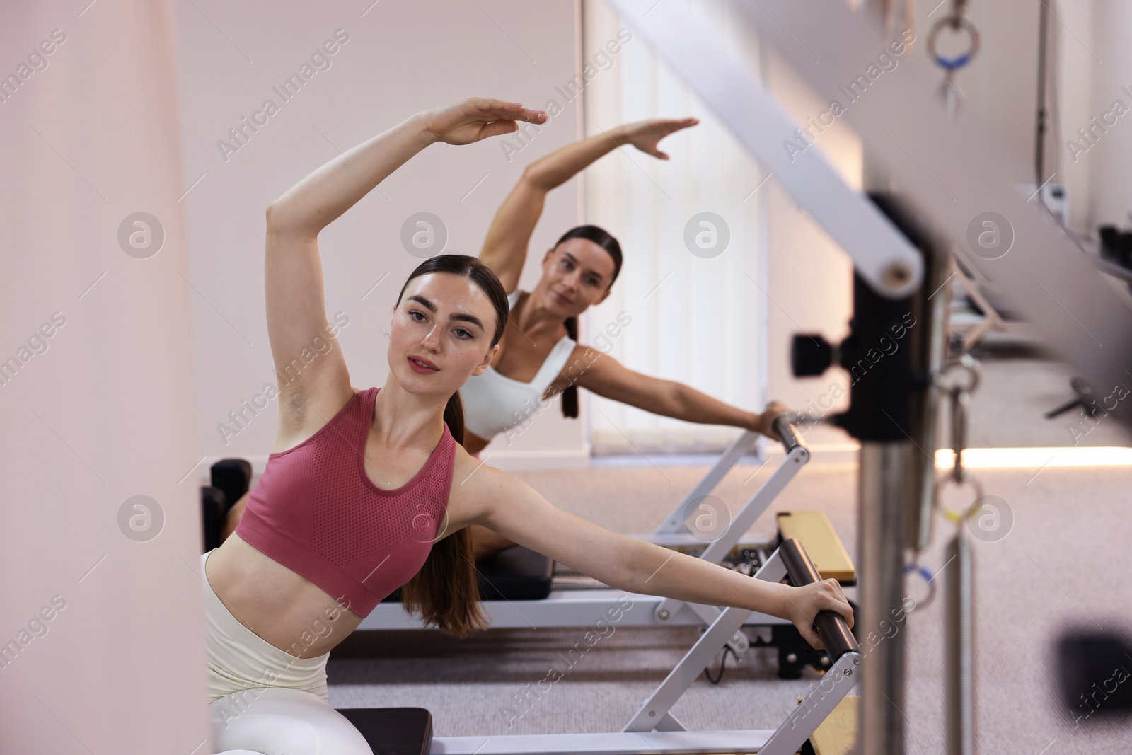 Photo of Woman and pilates instructor exercising on reformers in studio