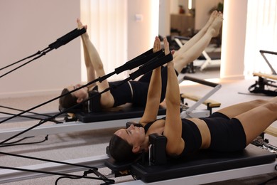 Photo of Woman and pilates instructor exercising on reformers in studio