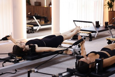 Photo of Woman and pilates instructor exercising on reformers in studio