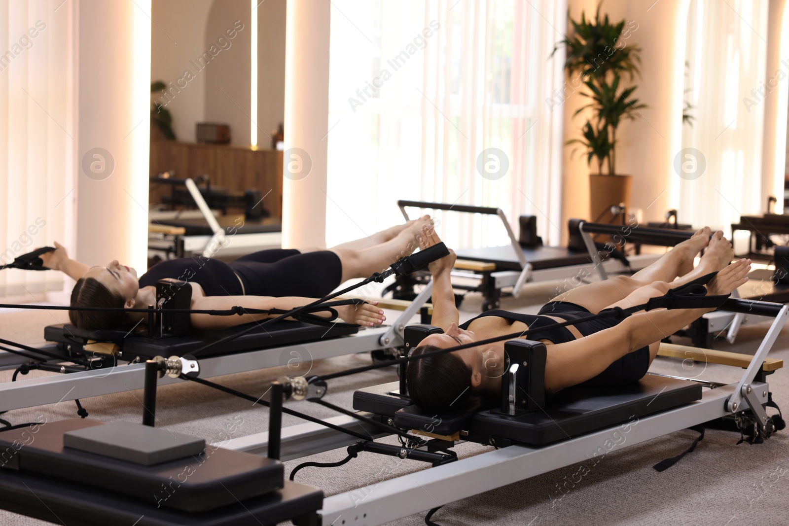 Woman and pilates instructor exercising on reformers in studio Photo of Woman and pilates instructor exercising on reformers in studio