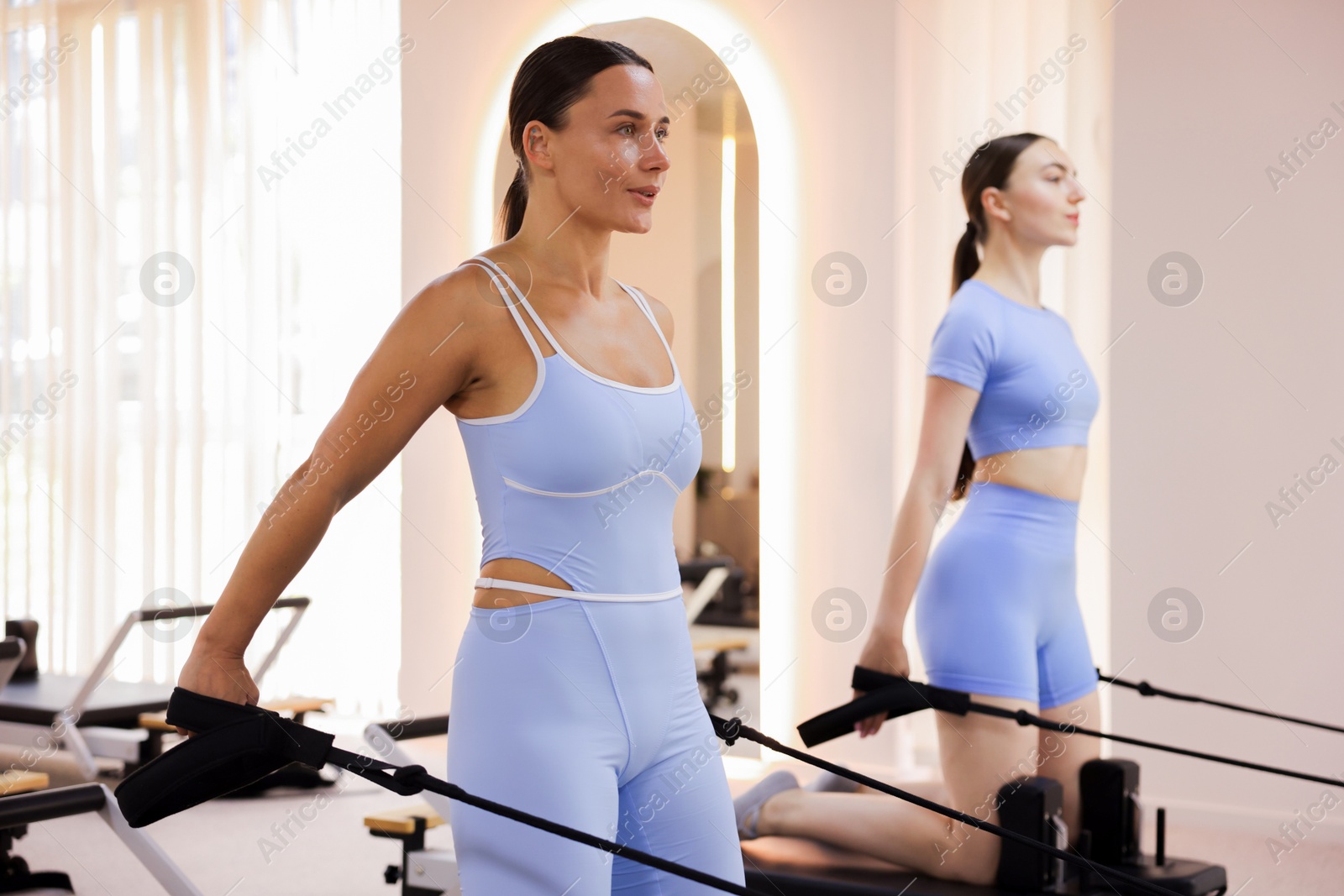 Photo of Woman and pilates instructor exercising on reformers in studio