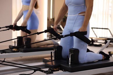 Photo of Woman and pilates instructor exercising on reformers in studio, closeup