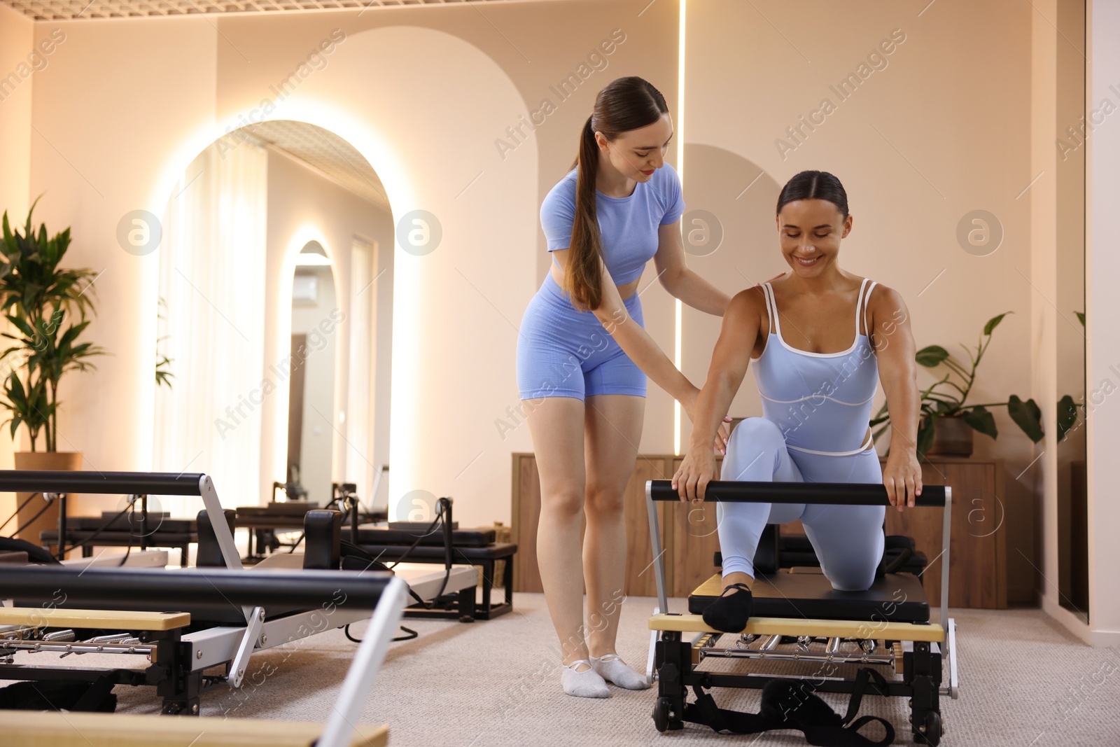 Photo of Woman exercising on reformer supervised by pilates instructor in studio, space for text