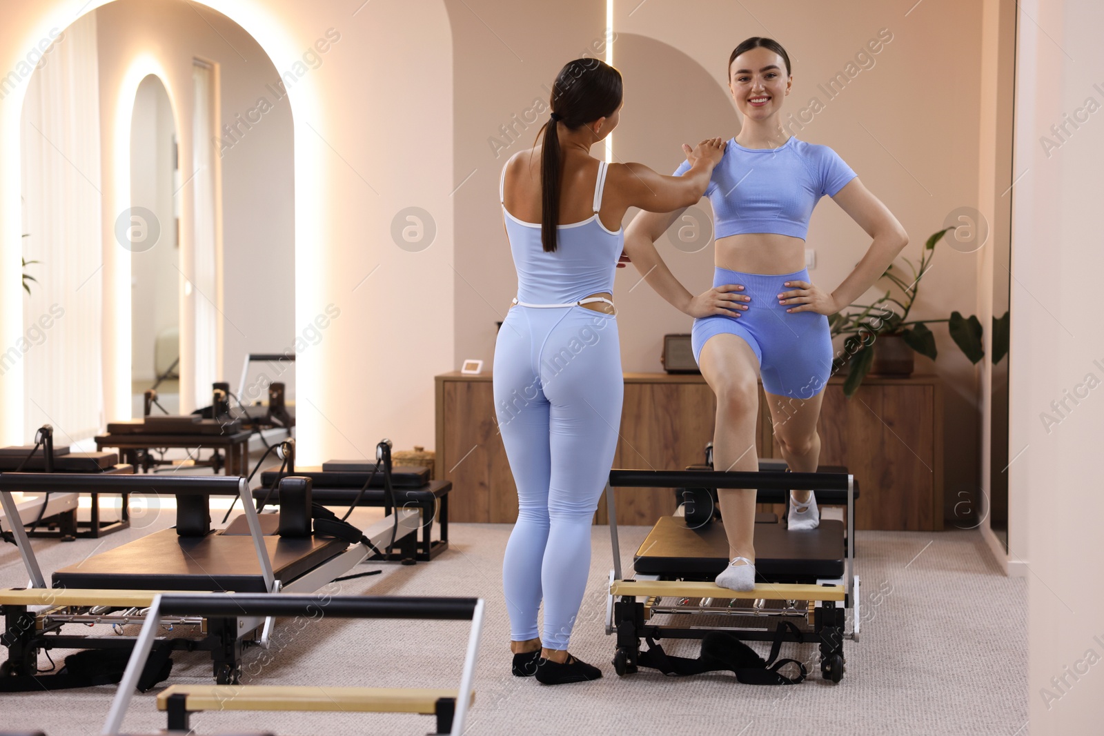 Photo of Woman exercising on reformer supervised by pilates instructor in studio