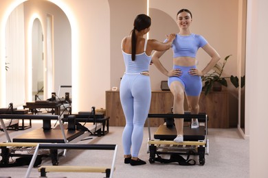 Photo of Woman exercising on reformer supervised by pilates instructor in studio
