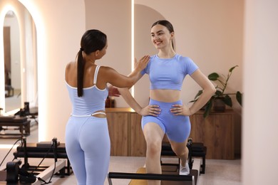 Photo of Woman exercising on reformer supervised by pilates instructor in studio