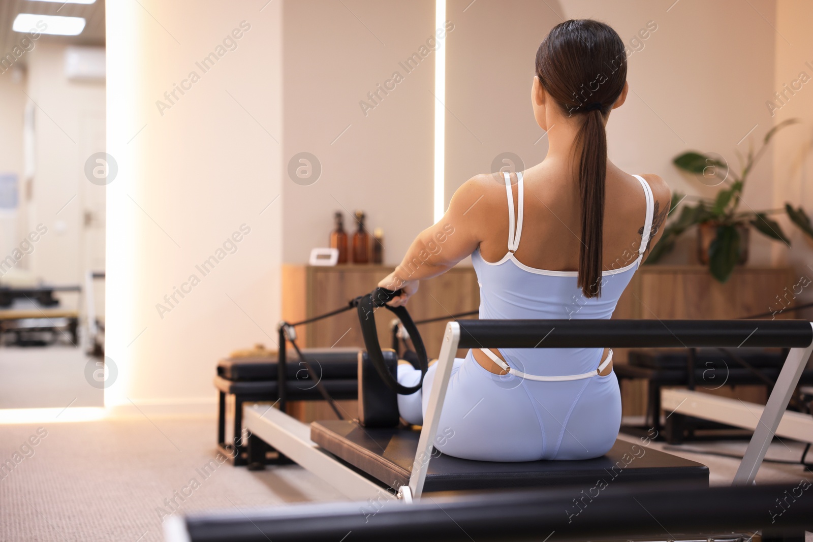 Photo of Woman exercising on reformer in pilates studio, back view. Space for text