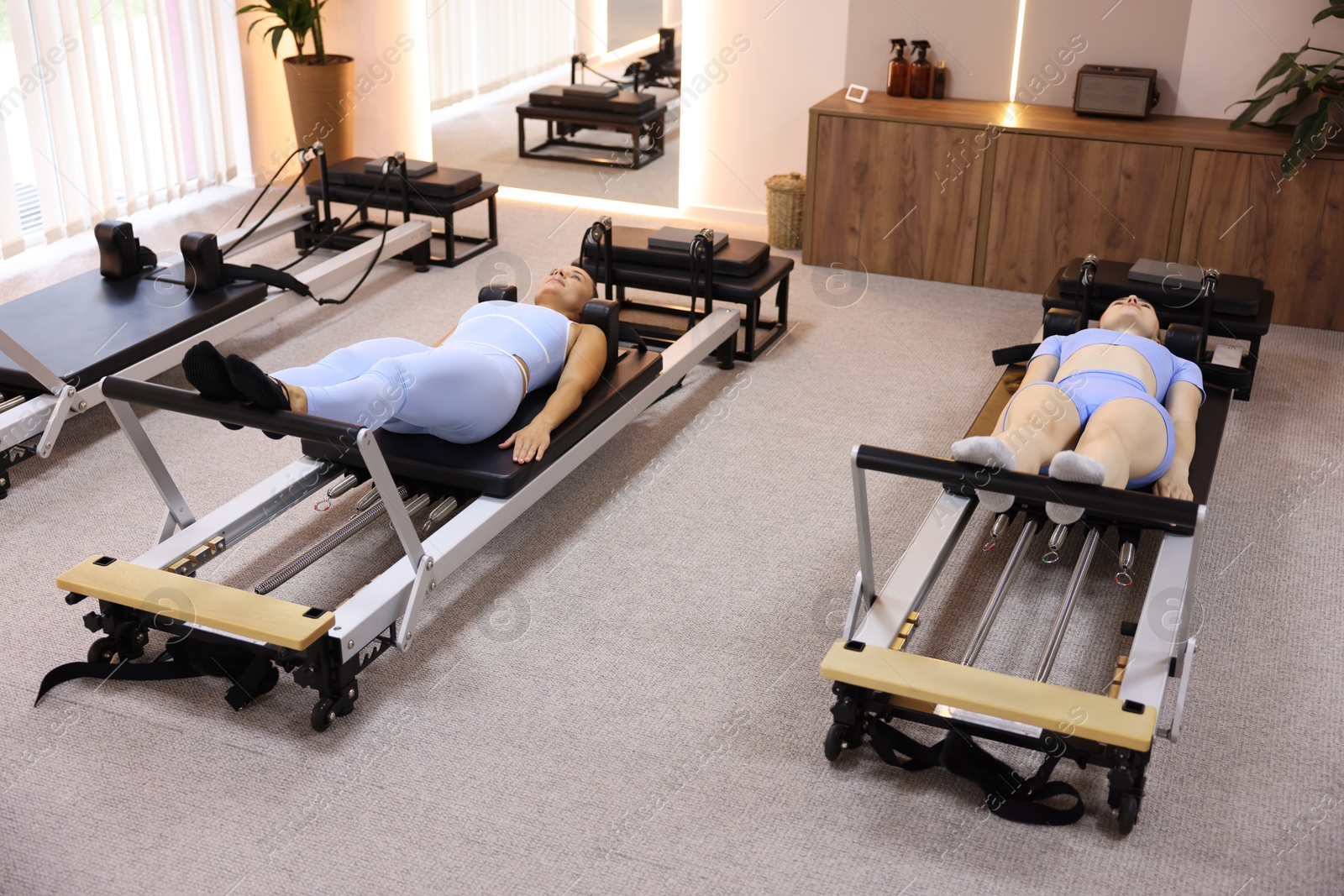 Woman and pilates instructor exercising on reformers in studio Photo of Woman and pilates instructor exercising on reformers in studio