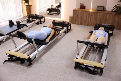 Photo of Woman and pilates instructor exercising on reformers in studio
