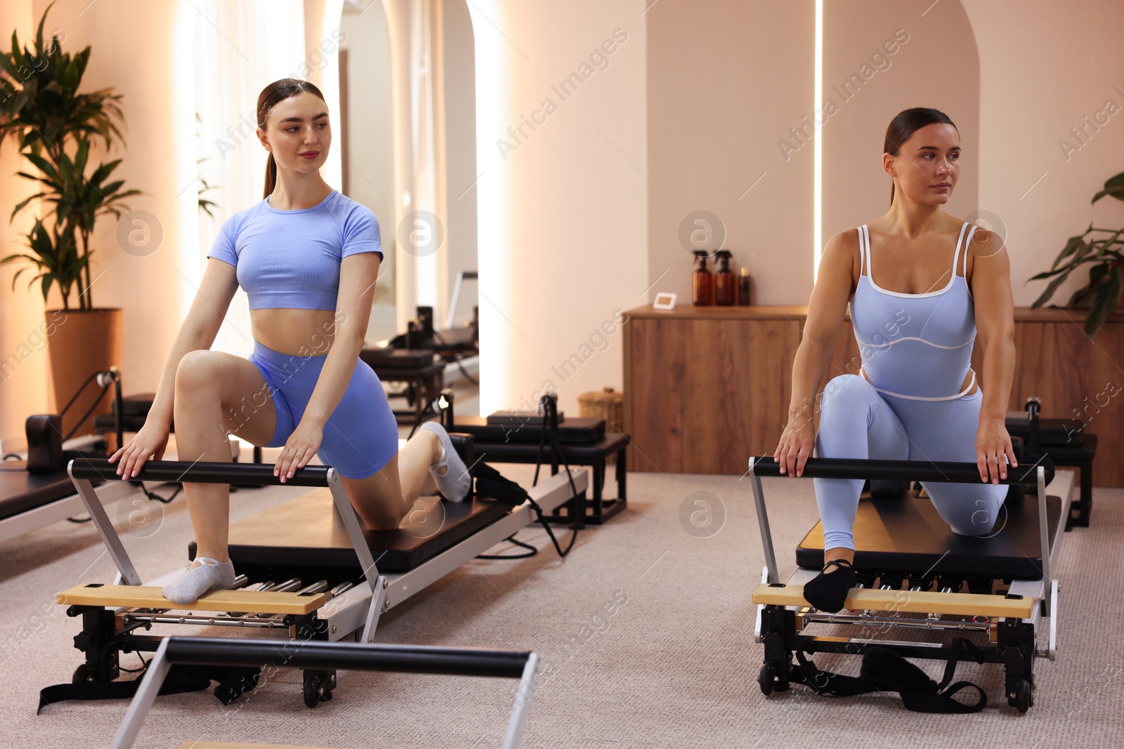 Woman and pilates instructor exercising on reformers in studio Photo of Woman and pilates instructor exercising on reformers in studio