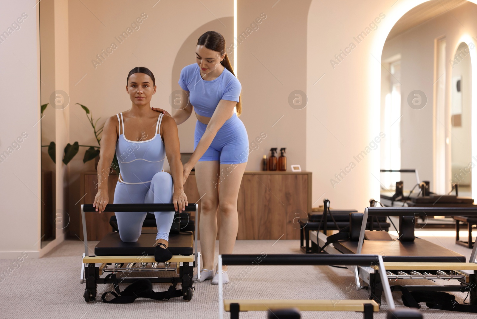 Photo of Woman exercising on reformer supervised by pilates instructor in studio, space for text