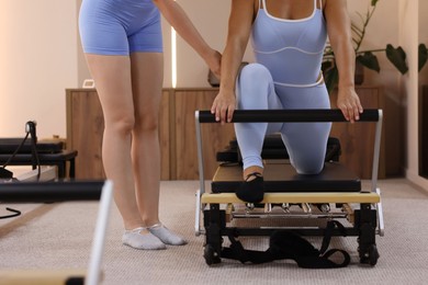 Photo of Woman exercising on reformer supervised by pilates instructor in studio, closeup