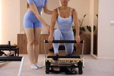 Photo of Woman exercising on reformer supervised by pilates instructor in studio, closeup