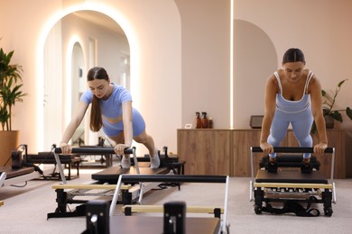 Photo of Woman and pilates instructor exercising on reformers in studio
