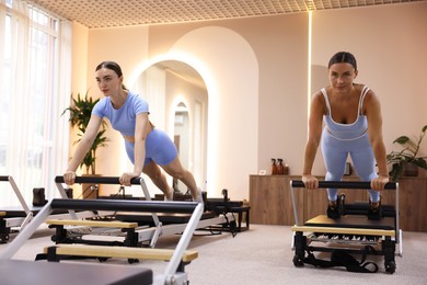 Photo of Woman and pilates instructor exercising on reformers in studio