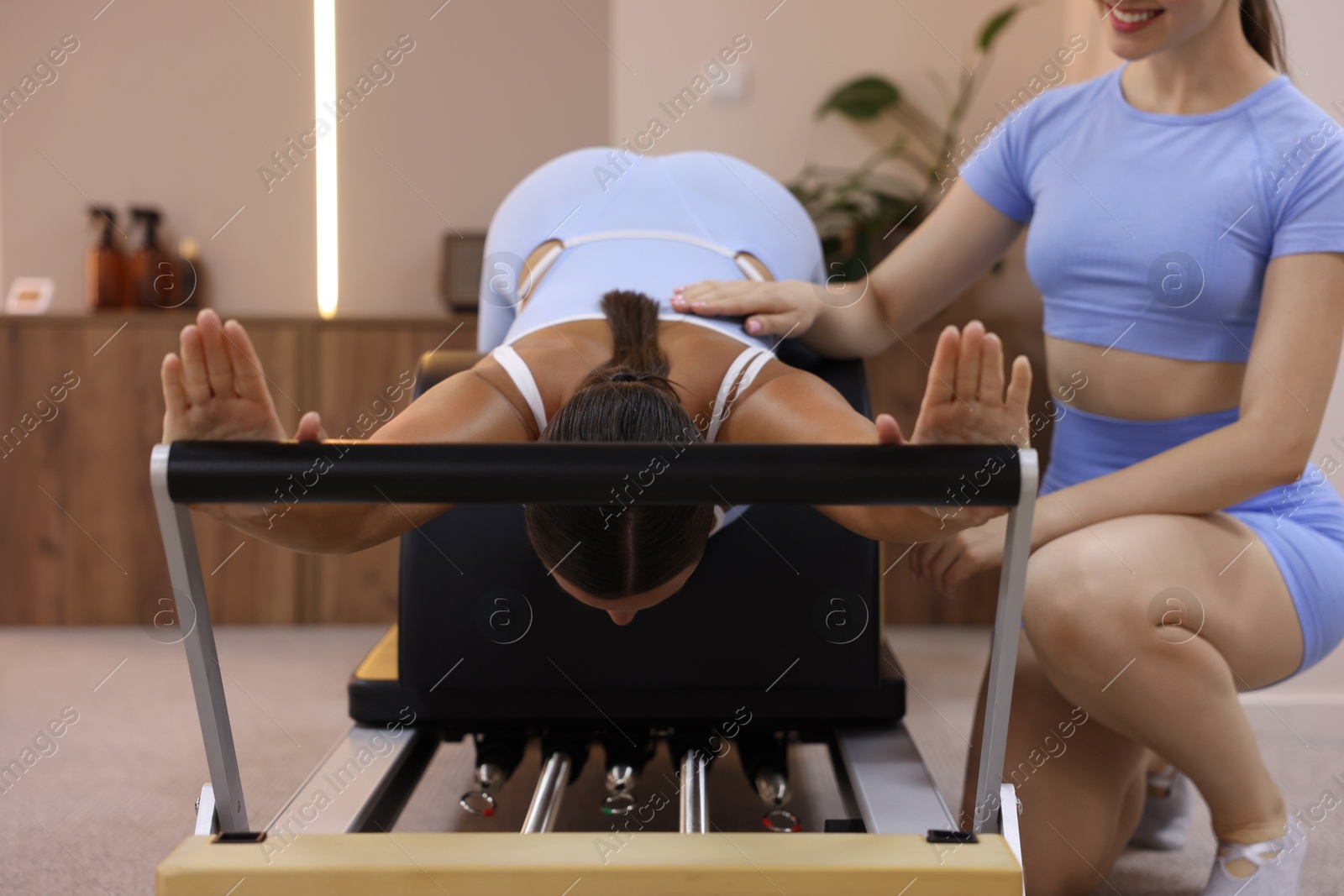 Woman exercising on reformer supervised by pilates instructor in studio Photo of Woman exercising on reformer supervised by pilates instructor in studio