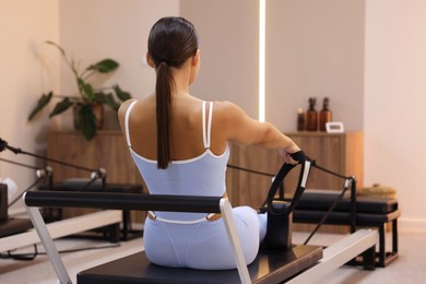 Photo of Woman exercising on reformer in pilates studio, back view