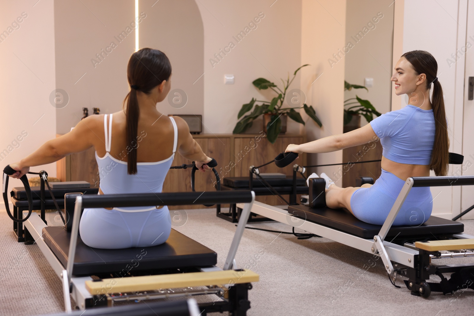 Woman and pilates instructor exercising on reformers in studio Photo of Woman and pilates instructor exercising on reformers in studio