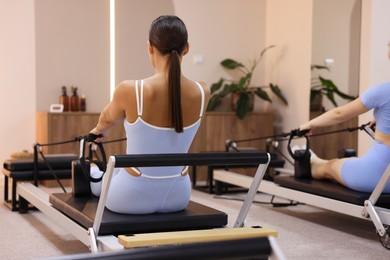 Photo of Woman and pilates instructor exercising on reformers in studio