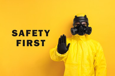 Image of Safety first, poster. Man in hazmat suit and gas mask showing stop gesture on orange background