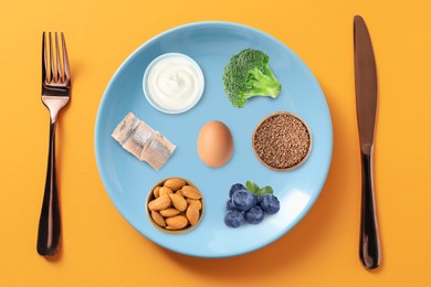 Image of Plate with collection of different foods and cutlery on orange background, top view. Healthy eating