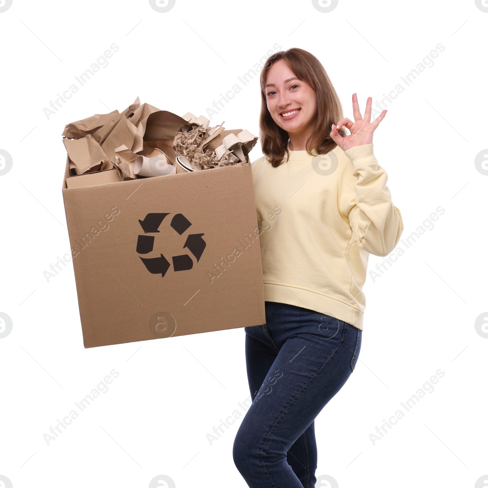 Photo of Recycling. Smiling woman holding cardboard box with different waste paper and showing OK gesture on white background