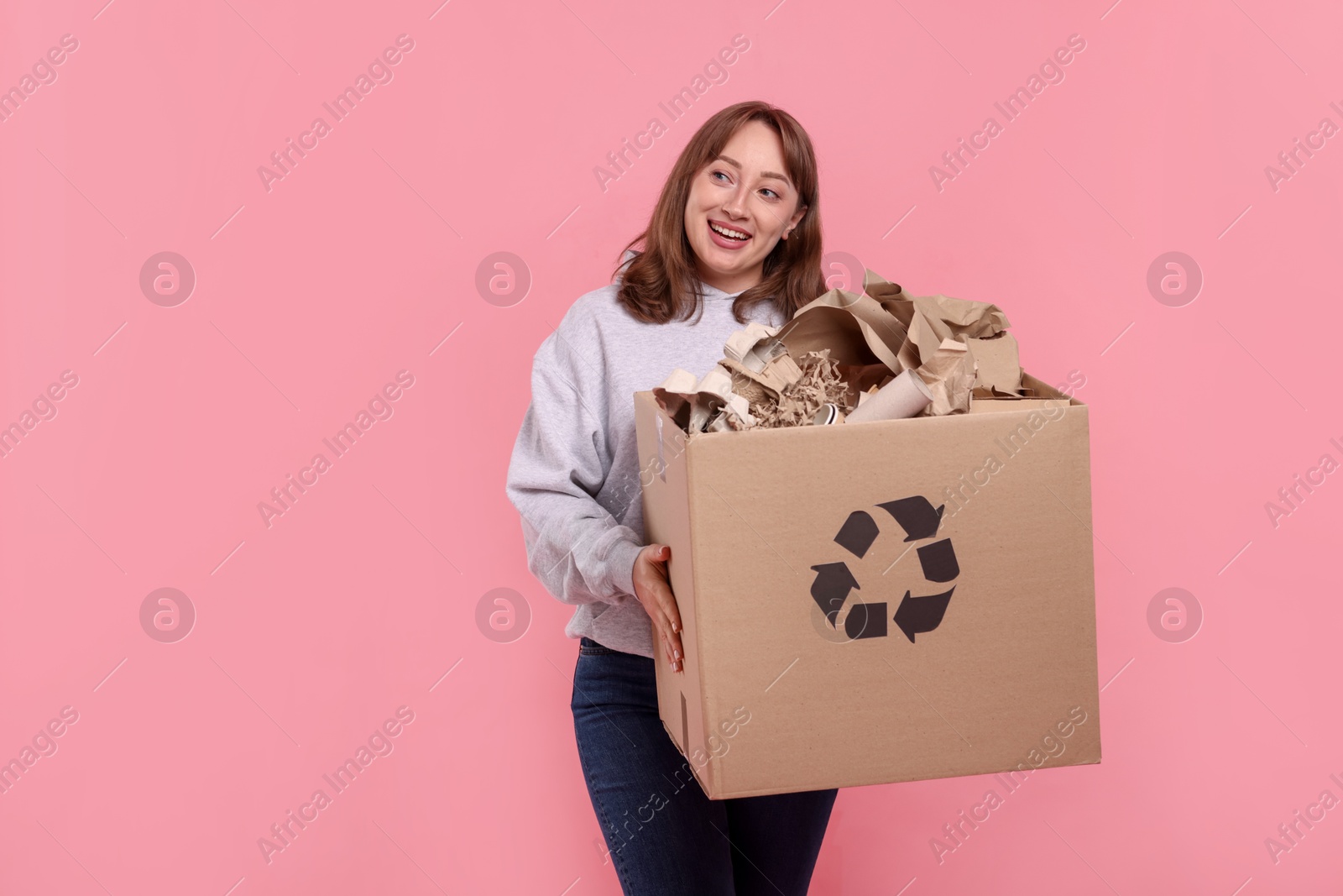 Recycling. Smiling woman holding cardboard box with different waste paper on pink background Photo of Recycling. Smiling woman holding cardboard box with different waste paper on pink background