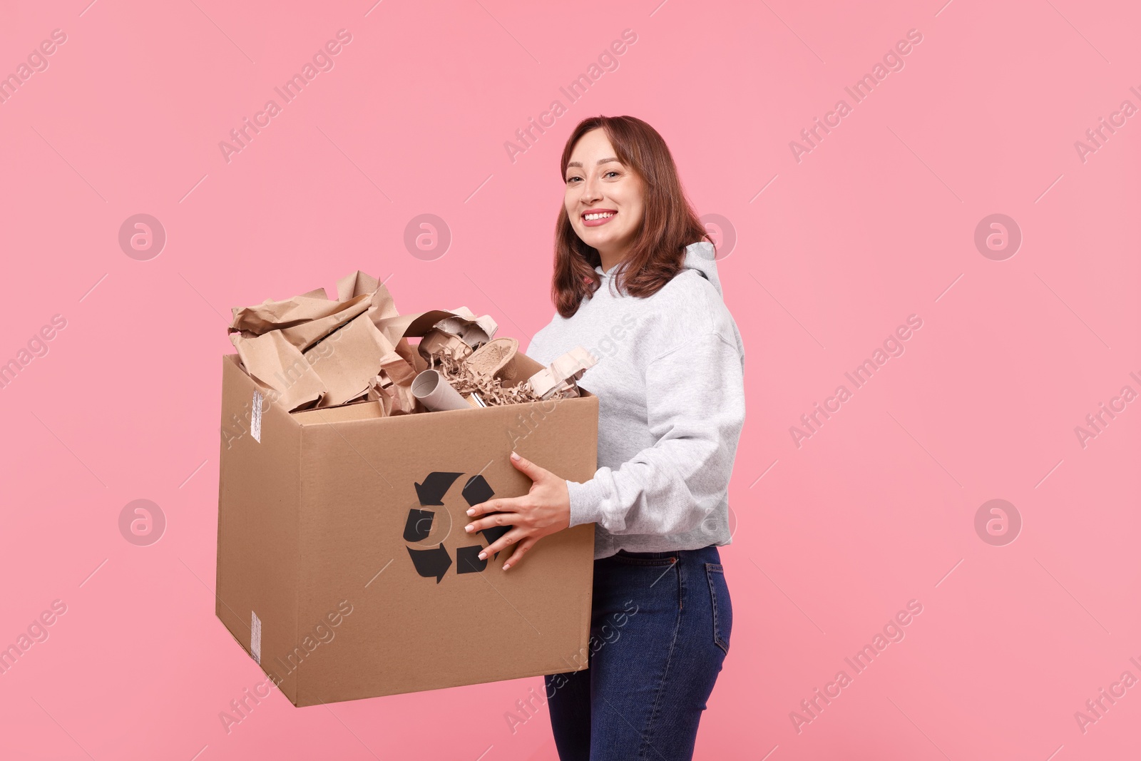 Photo of Recycling. Smiling woman holding cardboard box with different waste paper on pink background