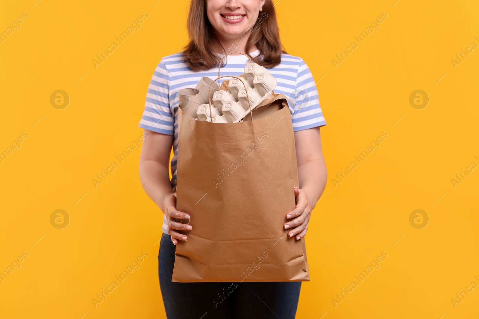 Photo of Recycling. Woman with bag full of different waste paper on yellow background, closeup