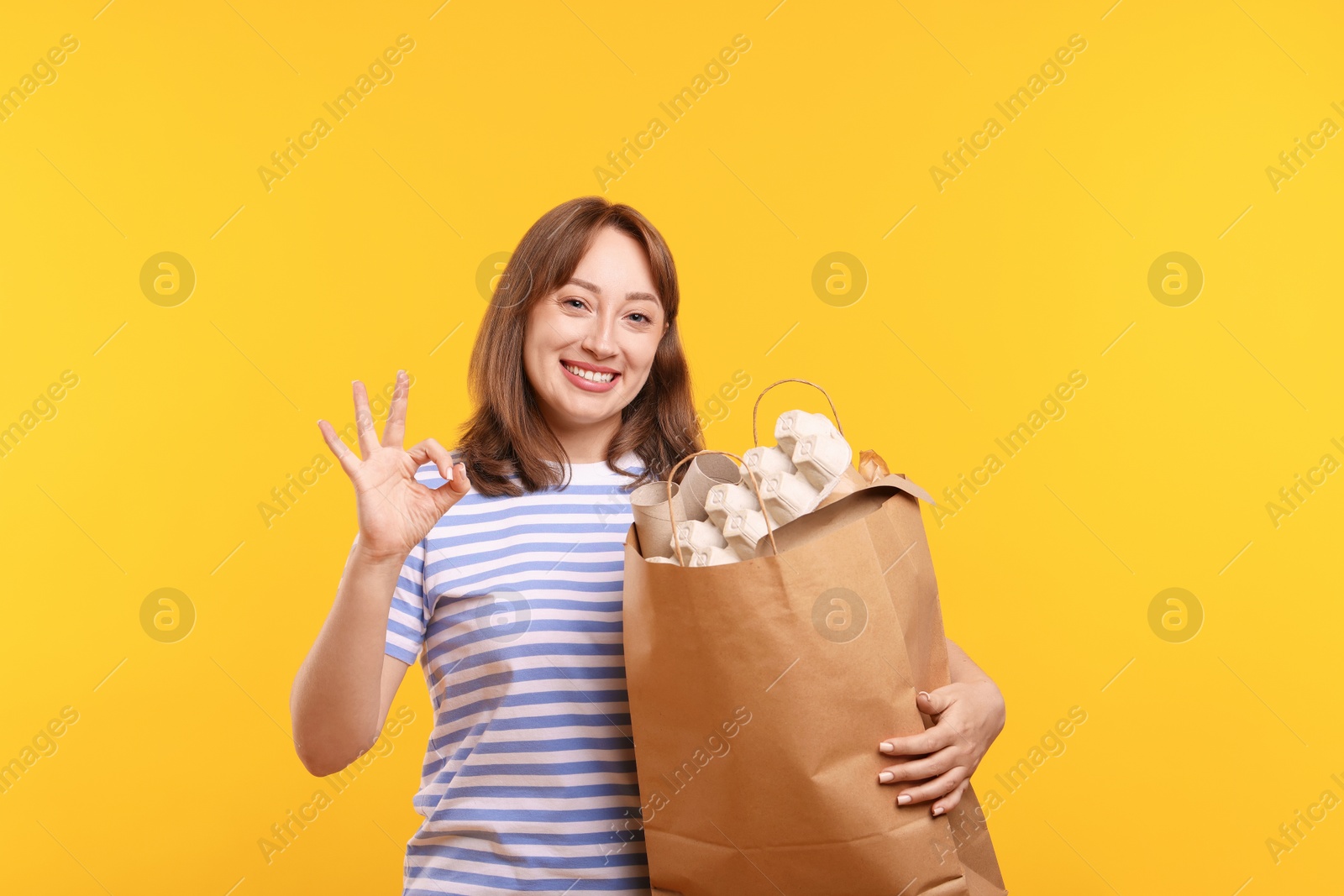 Photo of Recycling. Smiling woman with bag full of different waste paper showing OK gesture on yellow background