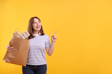 Photo of Recycling. Smiling woman with bag full of different waste paper pointing at something on yellow background. Space for text