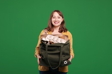 Photo of Recycling. Smiling woman with bag full of different waste paper on green background
