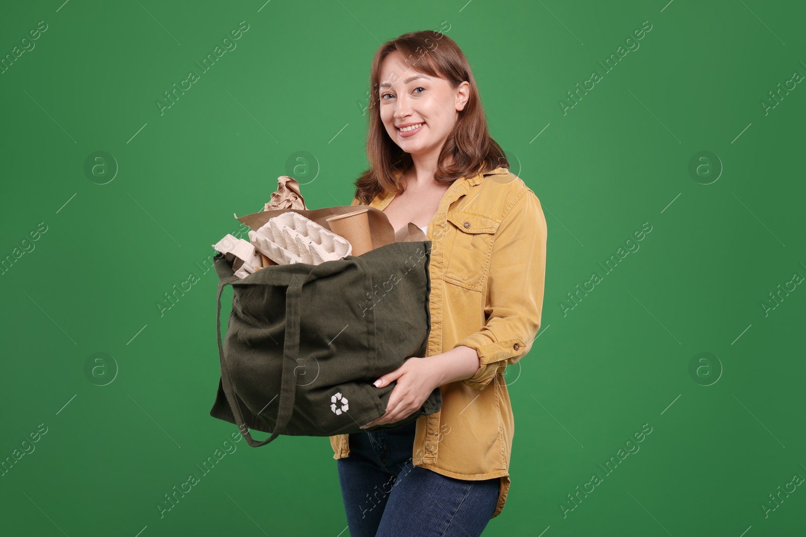 Photo of Recycling. Smiling woman with bag full of different waste paper on green background